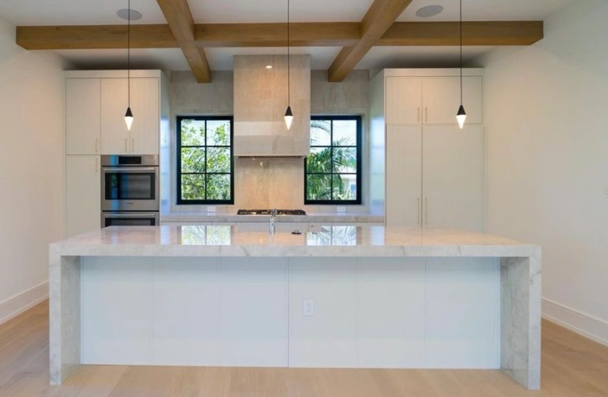 A kitchen with a marble waterfall island under exposed beams