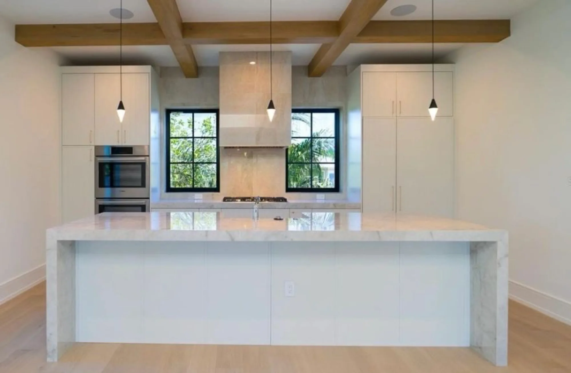 A kitchen with a marble waterfall island under exposed beams