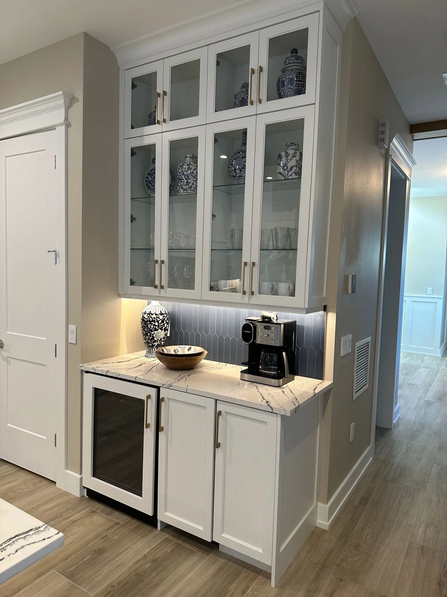 A glass front mini bar with a stone counter and under cabinet lighting